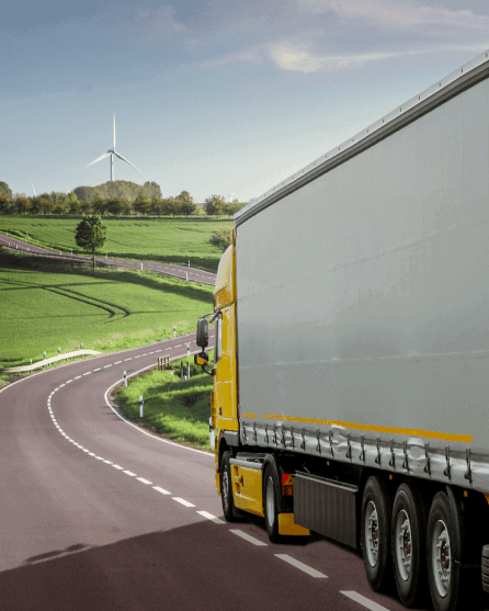 Yellow truck driving in the countryside with wind turbine in the distance